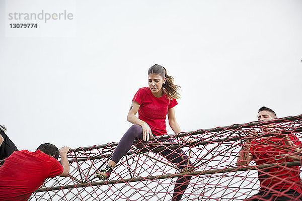 Niedrigwinkelansicht eines Mannes und einer Frau  die während des Rennens auf ein Netzhindernis klettern