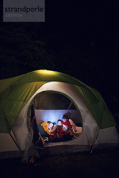 Freunde schauen auf digitales Tablet  während sie sich im Zelt entspannen