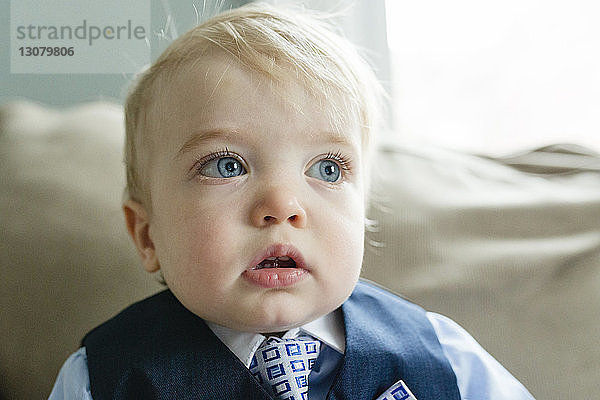 Nahaufnahme eines nachdenklichen kleinen Jungen im Anzug  der während der Osterfeierlichkeiten zu Hause auf dem Sofa wegschaut
