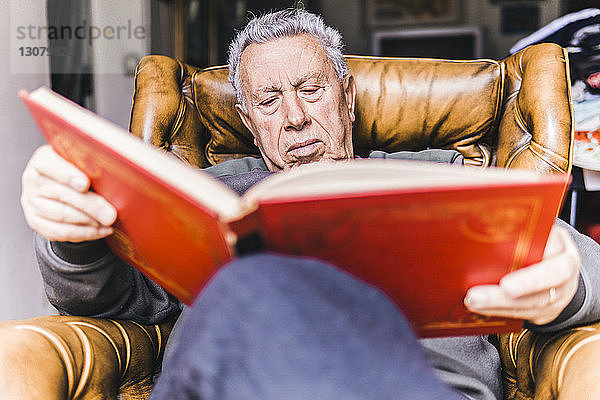 Niedriger Blickwinkel auf einen Mann  der ein Buch liest  während er zu Hause auf einem Sessel sitzt