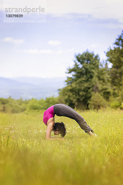Seitenansicht einer Frau  die Bridge-Posen-Yoga auf einem Grasfeld praktiziert