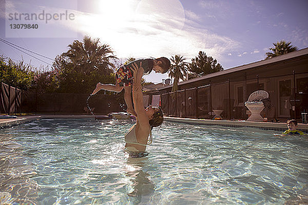 Glückliche Mutter hebt Jungen im Schwimmbad eines Touristenortes