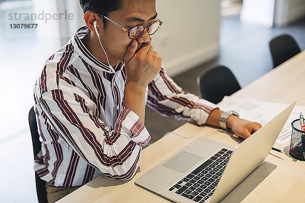 Hochwinkelansicht eines Geschäftsmannes mit der Hand bedecktem Mund bei der Arbeit am Laptop-Computer im Büro