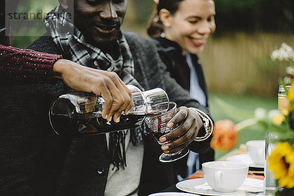 Ausgeschnittenes Bild eines Mannes  der Wein für einen Freund im Glas ausschenkt