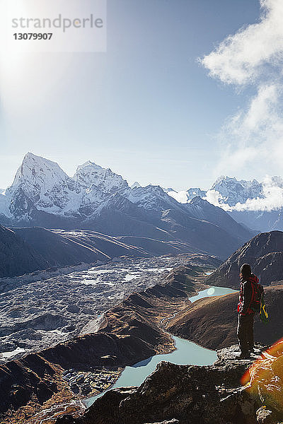 Seitenansicht eines Wanderers mit Rucksack  der am sonnigen Tag die Berge vor blauem Himmel betrachtet