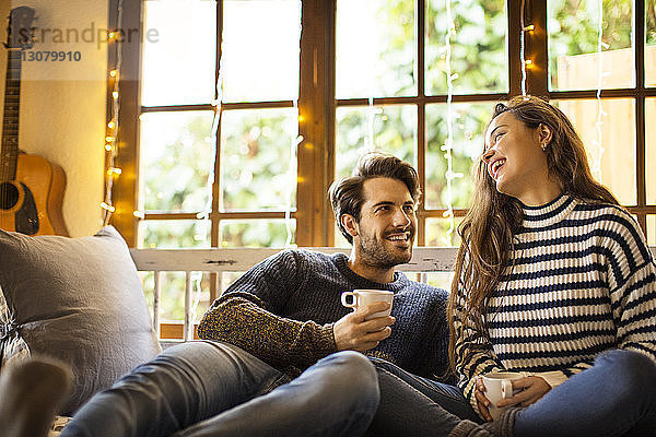 Glückliches Paar trinkt Kaffee  während es zu Hause auf einem Fensterplatz in einer Nische sitzt