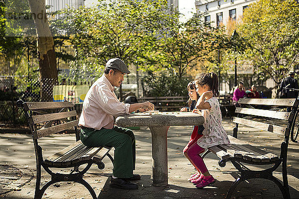 Seitenansicht von Großvater und Enkelinnen beim Spiel auf einer Parkbank sitzend