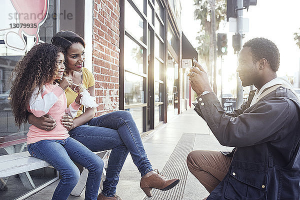 Glückliche Frau und Tochter posieren  während der Mann sie per Handy fotografiert