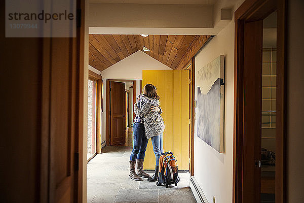 Umarmung von Tochter und Mutter in voller Länge am Eingang des Hauses