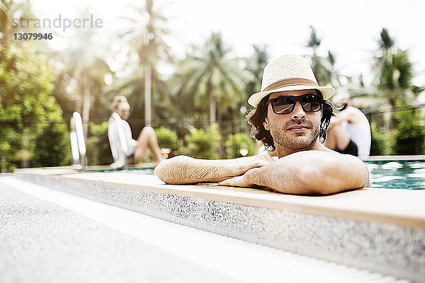 Nachdenklicher Mann entspannt sich im Schwimmbad mit Freunden im Hintergrund