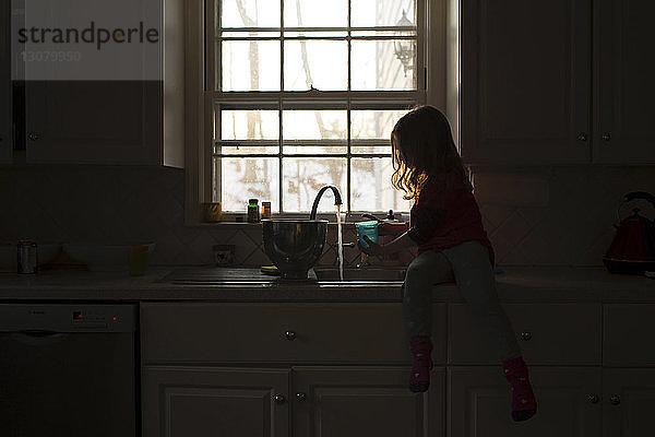 Mädchen spielt mit Wasser an der Küchenspüle