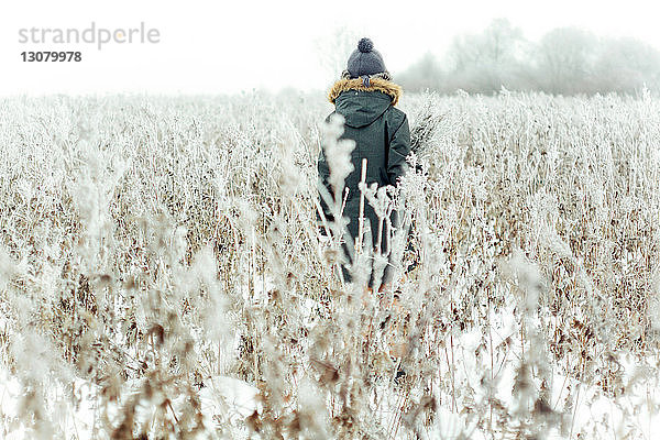 Rückansicht einer Frau  die im Winter inmitten von Pflanzen auf dem Feld steht