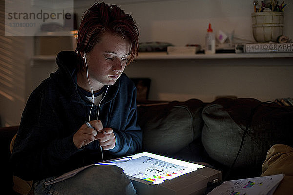 Teenagerin benutzt Tablet-Computer  während sie zu Hause auf dem Sofa sitzt