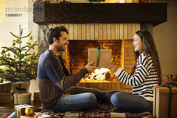 Glückliches Paar hält Weihnachtsgeschenk am Kamin zu Hause
