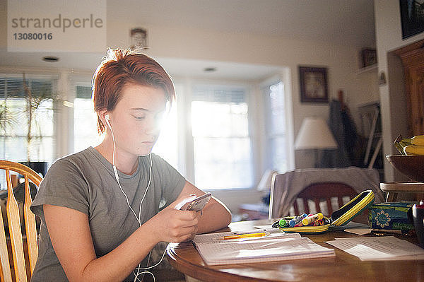 Teenagerin benutzt Mobiltelefon  während sie zu Hause auf einem Stuhl sitzt