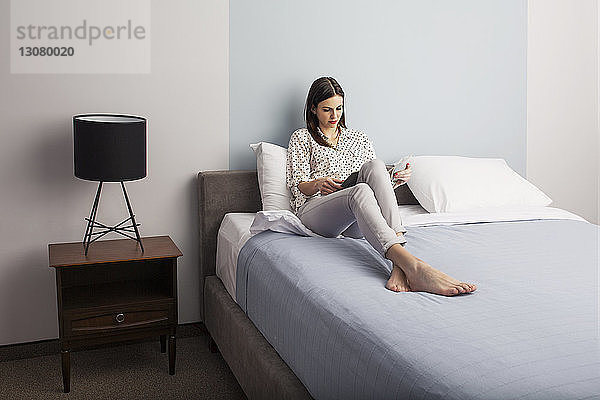 Geschäftsfrau liest Zeitschrift  während sie im Hotelzimmer auf dem Bett sitzt