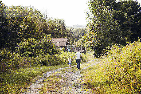 Rückansicht einer Enkelin mit Großvater  die auf einem Feldweg mitten im Gras geht