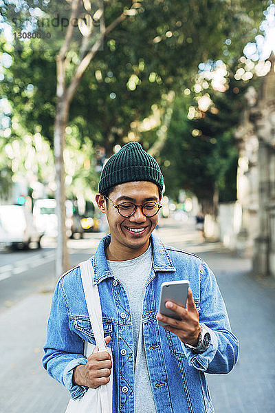Glücklicher Mann benutzt Smartphone  während er am Bürgersteig steht