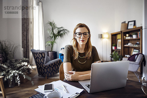 Porträt einer selbstbewussten Geschäftsfrau am Tisch sitzend mit Laptop im Büro