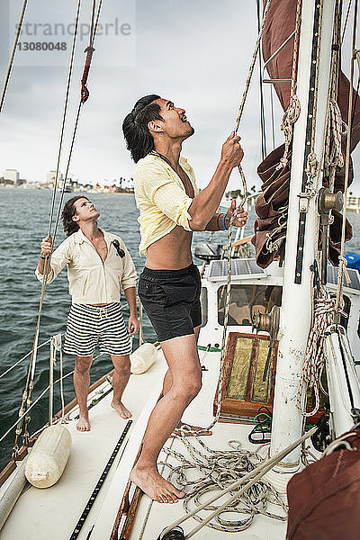 Mann verstellt Mast  während Freund im Segelboot reist