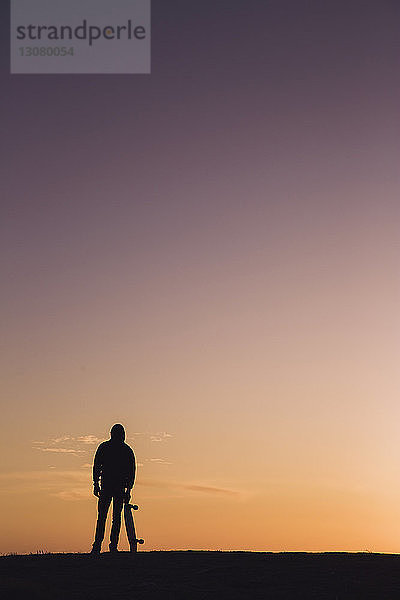 Scherenschnittmann mit Skateboard steht bei Sonnenuntergang vor dramatischem Himmel