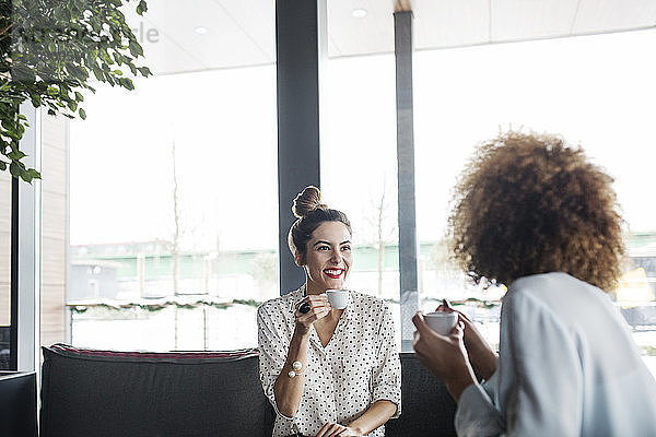 Glückliche Geschäftsfrau sieht ihren Kollegen an  während sie im Café eine Kaffeetasse hält