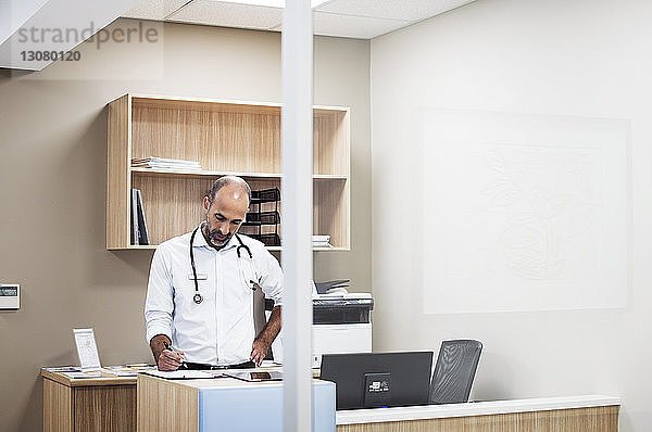 Arzt mit Hand an der Hüfte bei der Arbeit im Stehen im Krankenhauszimmer