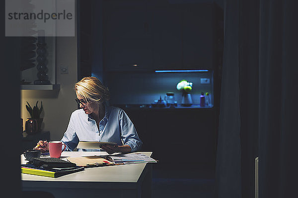 Geschäftsfrau nutzt Technologien  während sie am Schreibtisch im Heimbüro sitzt