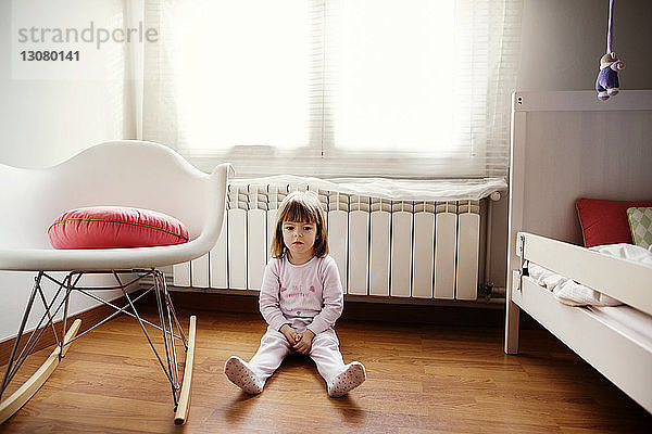 Nachdenkliches Mädchen auf Hartholzboden im Schlafzimmer sitzend