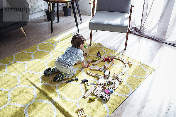 Hochwinkelaufnahme eines kleinen Jungen  der zu Hause mit einer Spielzeugeisenbahn spielt