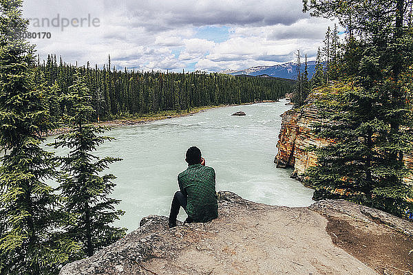 Mann betrachtet Aussicht  während er auf einer Klippe im Jasper-Nationalpark sitzt