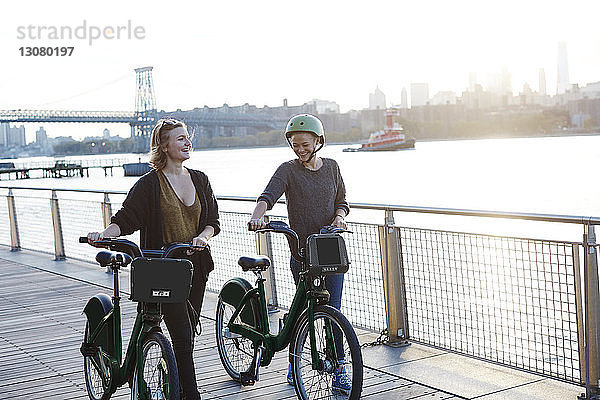 Lächelnde Freunde mit Fahrrädern auf der Promenade am Fluss