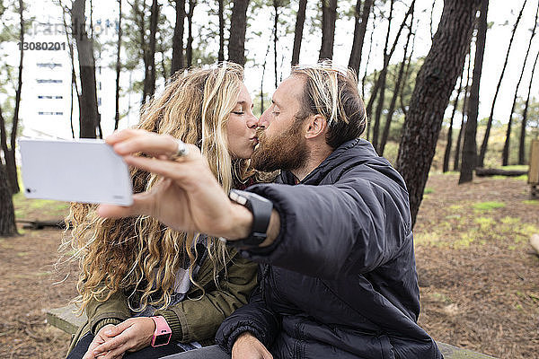 Romantisches Pärchen  das sich küsst  während es sich durch ein Smartphone im Wald durchsetzt