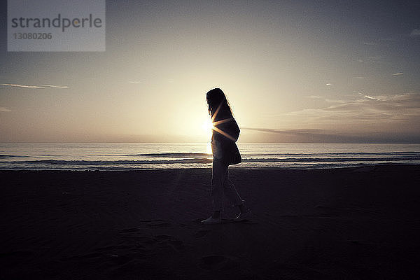 Seitenansicht einer Frau  die bei Sonnenuntergang am Meeresufer gegen den Himmel läuft