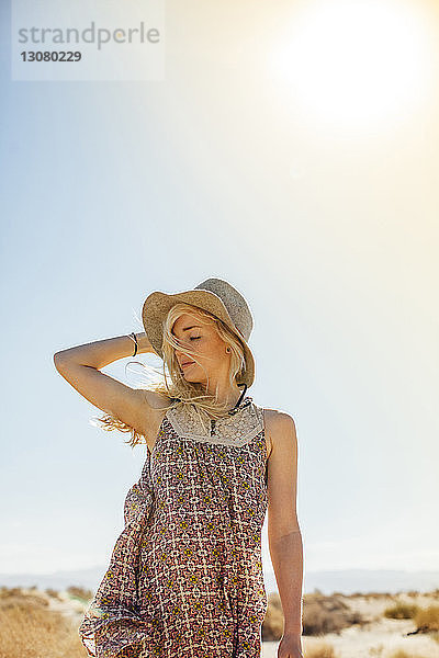 Frau mit Sonnenhut steht am sonnigen Tag vor klarem Himmel