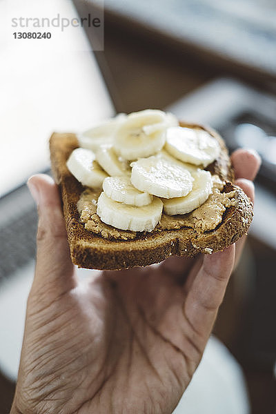 Abgehackte Hand eines Mannes  der zu Hause Brot mit Bananenscheiben hält