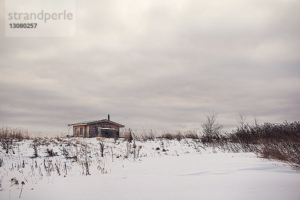 Haus auf schneebedecktem Feld vor bewölktem Himmel