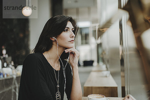 Nachdenkliche Frau  die Musik hört  während sie durch das Fenster eines Cafés schaut
