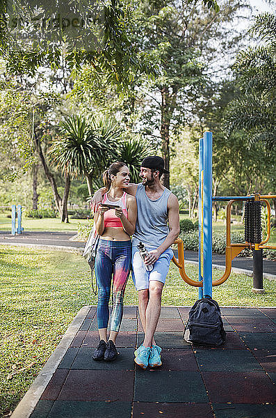 Frontansicht eines glücklichen Paares  das sich im Park über ein Fitnessgerät beugt