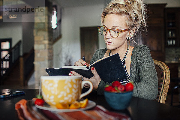 Frau schreibt Tagebuch  während sie am Frühstückstisch sitzt