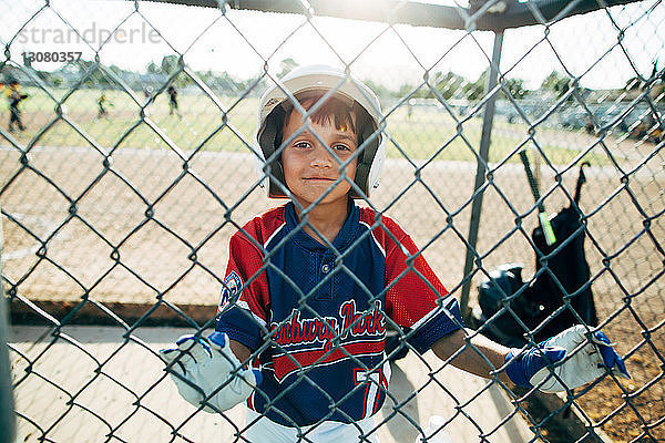 Porträt eines glücklichen Baseball-Spielers  der hinter einem Maschendrahtzaun steht