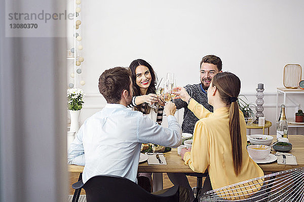 Glückliche Freunde stoßen beim Mittagessen am Esstisch auf Champagnerflöten an