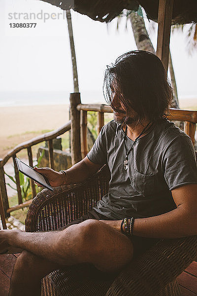 Mann benutzt Tablet-Computer  während er am Strand sitzt