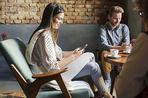 Geschäftsfrau benutzt Smartphone  während sie mit Kollegen in der Hotellobby sitzt