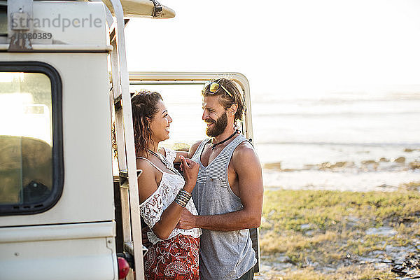 Fröhliches Paar steht bei Geländewagen am Strand vor klarem Himmel