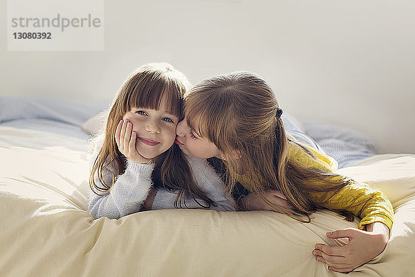 Mädchen küsst Schwester beim Entspannen zu Hause im Bett