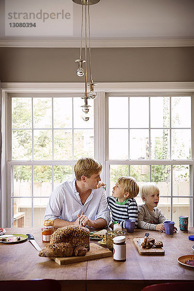 Vater und Söhne essen am Tisch vor dem Fenster
