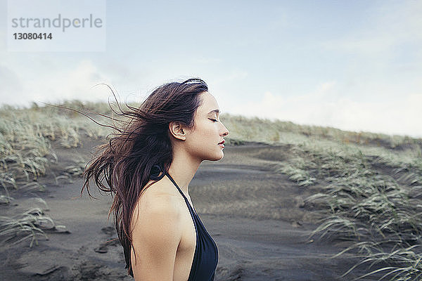 Seitenansicht einer Frau  die am Bethells Beach eine Brise gegen den Himmel genießt