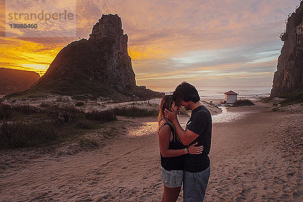 Seitenansicht eines romantischen Paares  das bei Sonnenuntergang am Strand steht