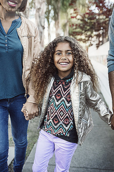 Porträt eines glücklichen Mädchens  das mit seinen Eltern auf dem Bürgersteig geht